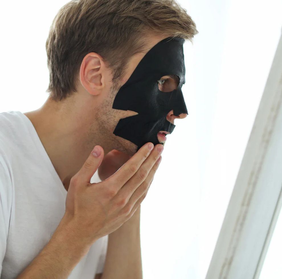 Man wearing a black mask and looking into a mirror.